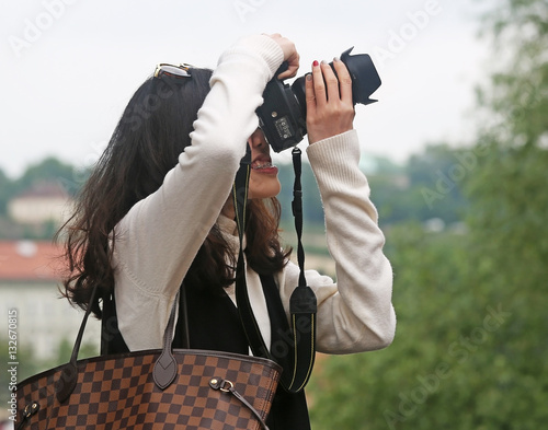 Азиатская девушка фотограф в белом свитере с клетчатой сумкой и цифровым зеркальным фотоаппаратом