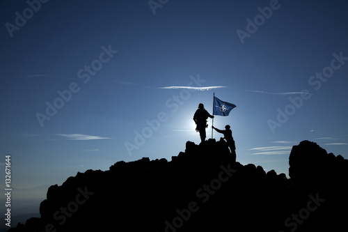 Two soldiers put the NATO flag on top of the mountain photo