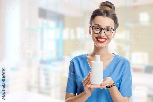 Portrait of a young smiling cosmetologist holding a bottle with cosmetics in the cosmetology room