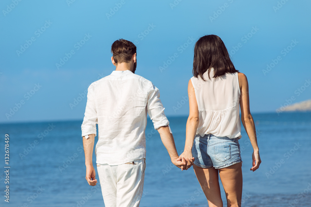 Couple walking on beach. Young happy interracial couple walking on beach smiling holding around each other. Couple walking on beach. Young happy interracial couple walking on beach smiling holding around each other.