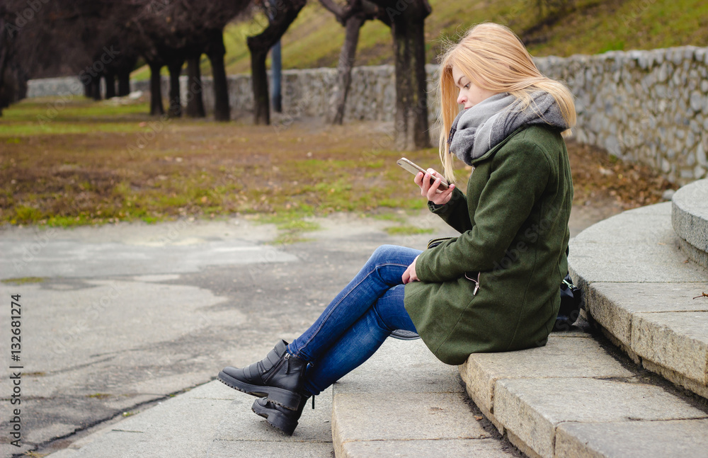 Girl on the street. Sitting on the steps. Cool day. Phone in hand. Girl is typing a message. For content to the site Girl on the street. Sitting on the steps. Cool day. Phone in hand. Girl is typing a message. For content to the site