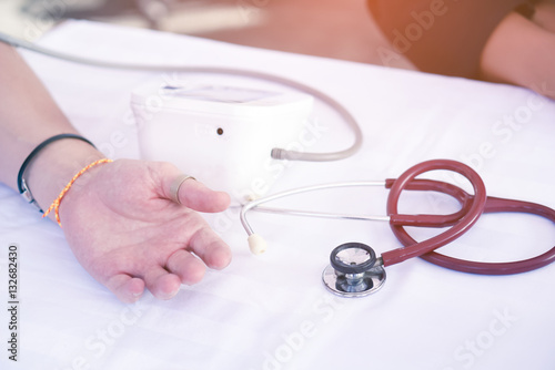 Patient checking his blood pressure with an electrical sphygmomanometer (blood pressure monitor) and a red stethoscope at a hospital waiting room