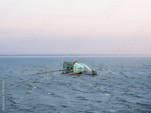 Shipwreck after an autumn storm overturned sailboat. Captain clings to the side of the boat. The Old Man and the Sea.