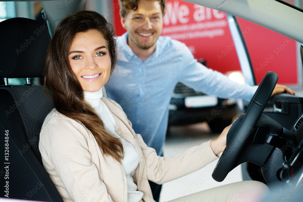 Beautiful young couple looking a new car at the dealership showroom Beautiful young couple looking a new car at the dealership showroom