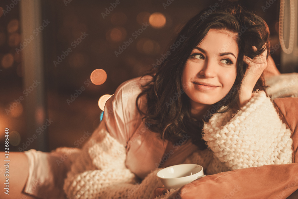 Fototapeta premium Portrait of beautiful young woman with cup of hot drink in cozy home interior