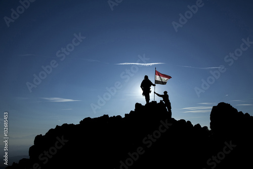 Canvas Print Two soldiers raise the Iraqi flag on top of the mountain