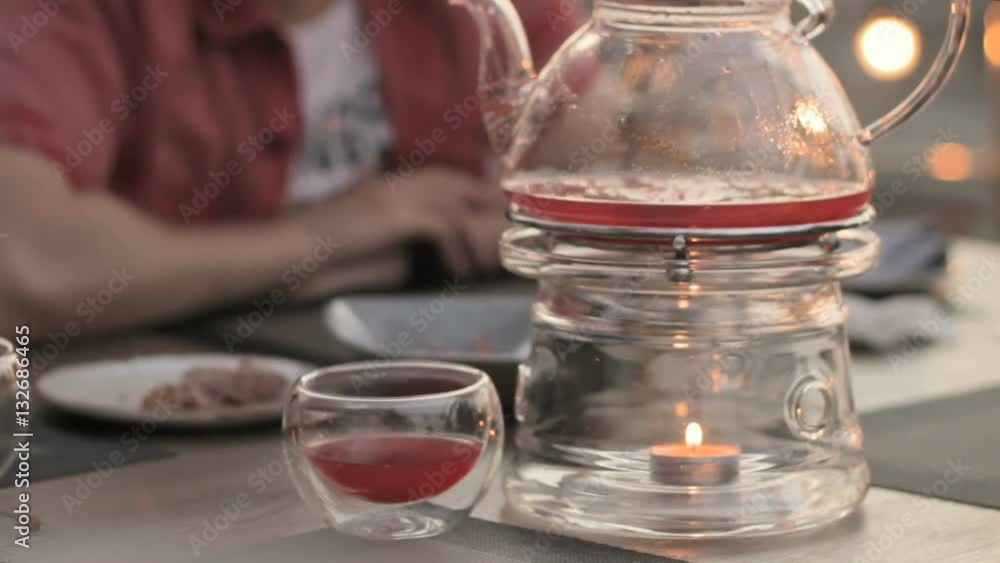 People in the cafe, transparent teapot on a table with candles heated People in the cafe, transparent teapot on a table with candles heated
