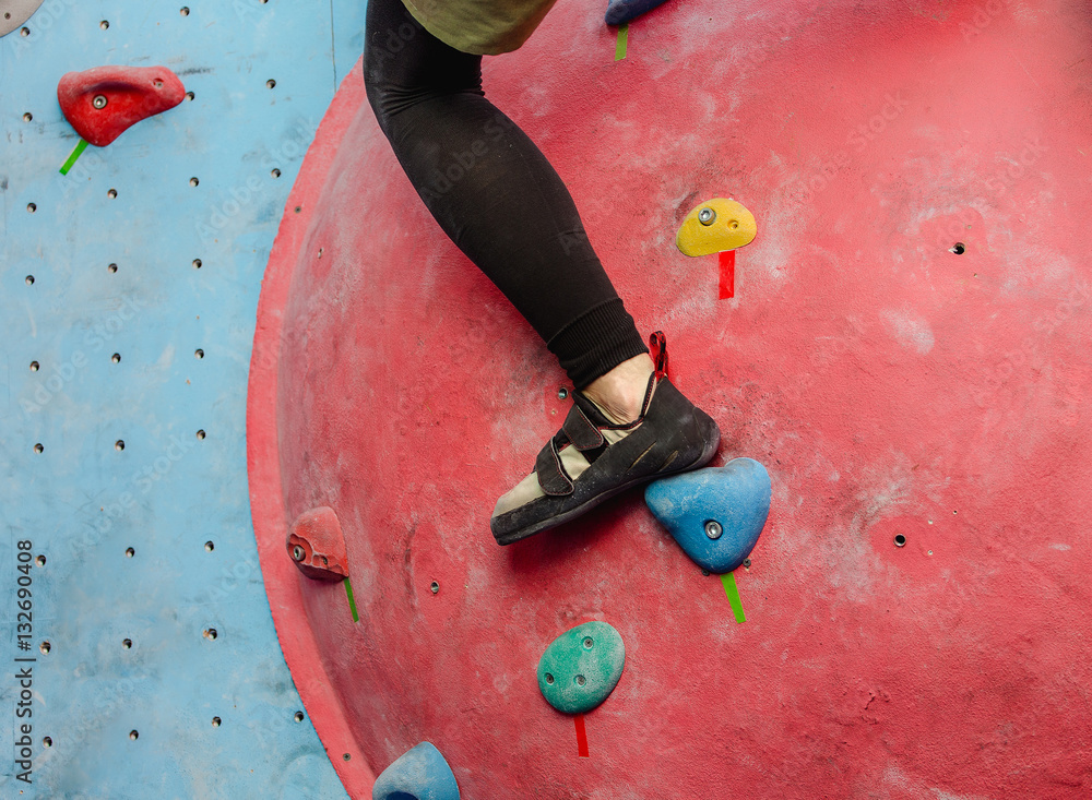 Foot with shoes of female climber on artificial boulder wall at gym