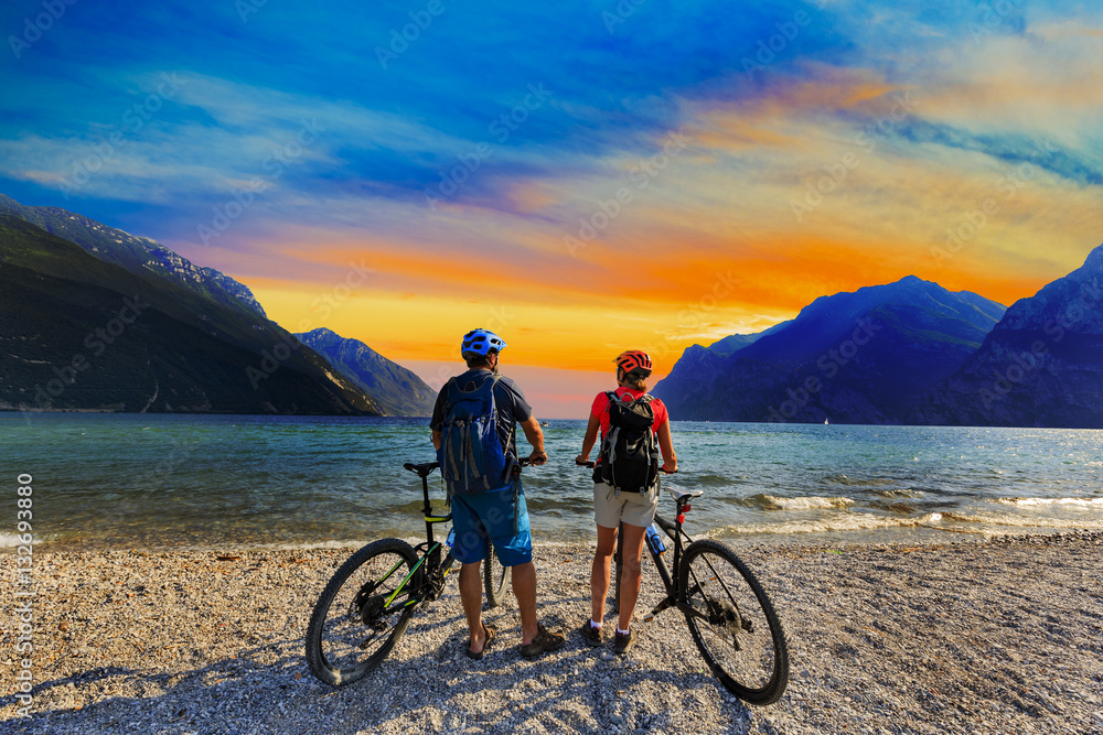 Fototapeta premium Mountain biking, couple with bikes at sunset on Lake Garda, Riva