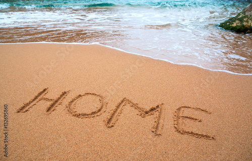 written words " home " on sand of beach with wave on background