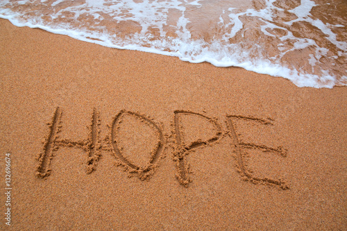 written words " hope " on sand of beach with wave on background