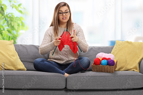 Confused young woman on a sofa knitting photo