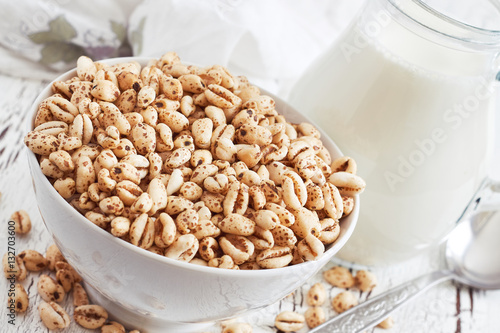 Obraz na plátně Puffed wheat cereal in white bowl with pitcher of milk in background