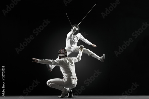 Fencers fencing, one fencer jumping in air photo