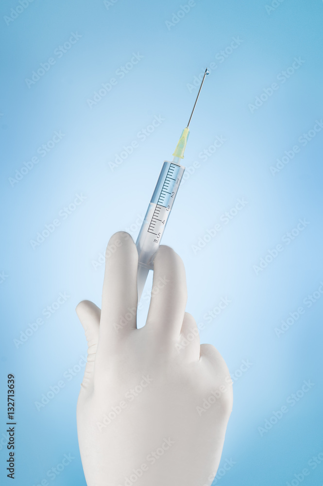 Doctors hand in white glove holding a syringe on a blue background. Injection or vaccination concept photograph with copy space. Doctors hand in white glove holding a syringe on a blue background. Injection or vaccination concept photograph with copy space.