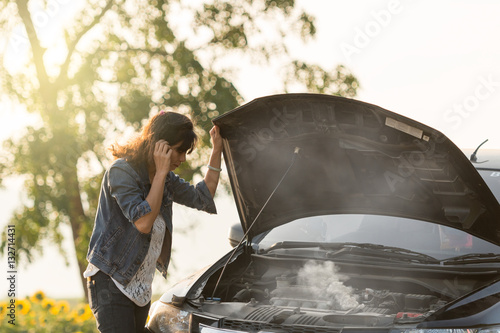 sad woman standing on the road by the broken car in the middle of nowhere. smoke coming out the engine. Help needed. Car service. Tow service.