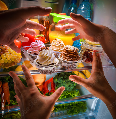 Human hands reaching for sweet cake at night in the open refrige photo