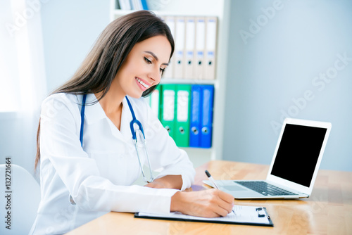 Portrait of happy young friendly doctor writing diagnosis
