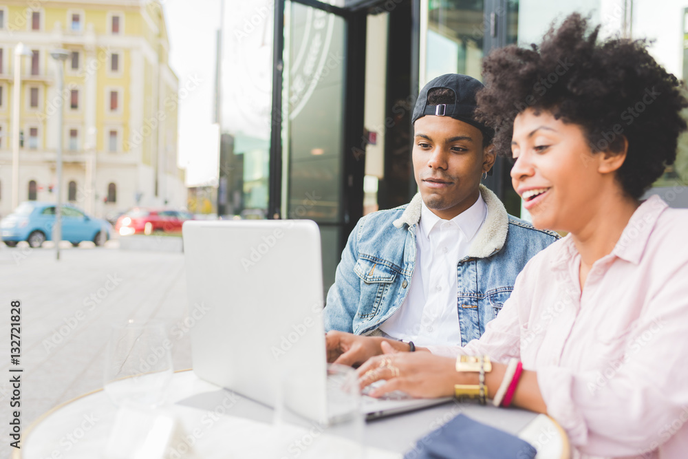 Young multiethnic couple using computer sitting outdoor in the city - business, technology, internet concept Young multiethnic couple using computer sitting outdoor in the city - business, technology, internet concept