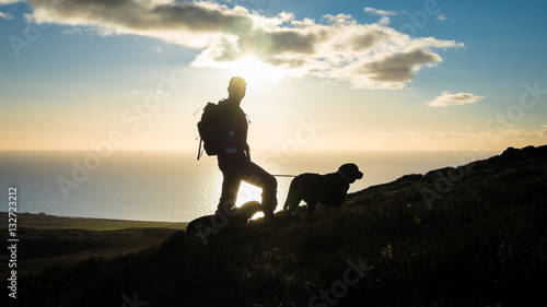 Silhouettes of a hiker and two dogs at Black Combe in the Lake District, with sunset over the Irish Sea