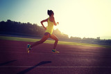 Young woman running during sunny morning on stadium track