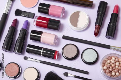 A collection of cosmetic make up products arranged on a pastel purple background