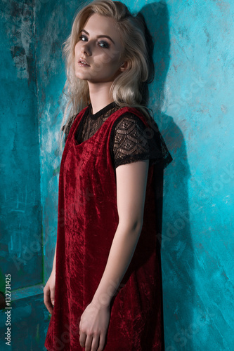 Beautiful blonde girl in a red dress posing against a wall green