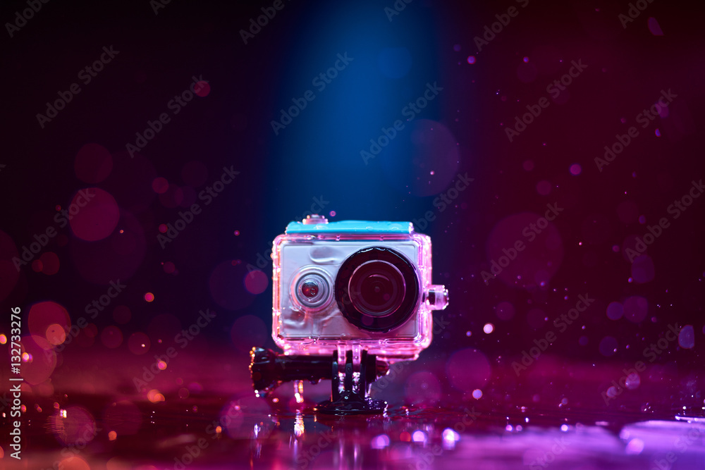 Naklejka premium Concept: gear, gadget, action lifestyle, millennial. Vivid colorful shot of action camera in waterproof case splashed with water. Time freeze.