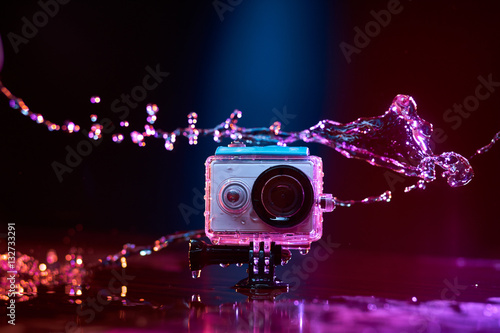Concept: gear, gadget, action lifestyle, millennial. Vivid colorful shot of action camera in waterproof case splashed with water. Time freeze.