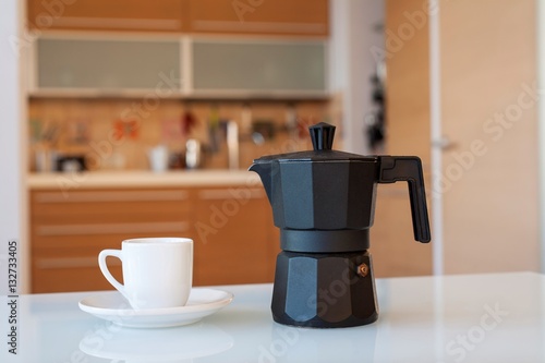 чашка и кофейник на столе на фоне кухни