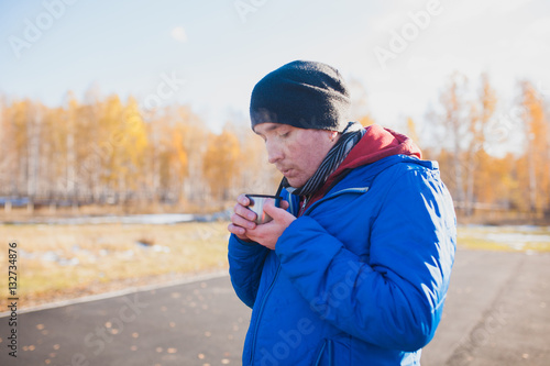 Young man on a walk in the park drinking tea from a mug from a thermos.
