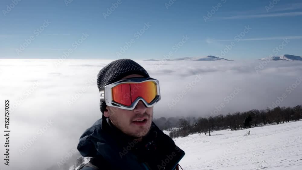 Man in Snow Mask is Making Selfie While Winter Hike Above the Clouds With a View of the Distant Peaks by a Coast of the Cloud Sea