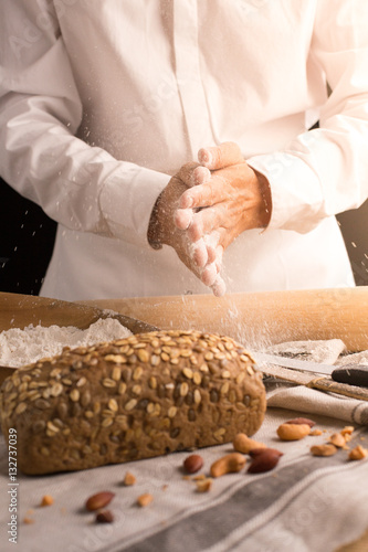 A male chef's hand present and cutting whole grain bread with gold knife and pouring flour.