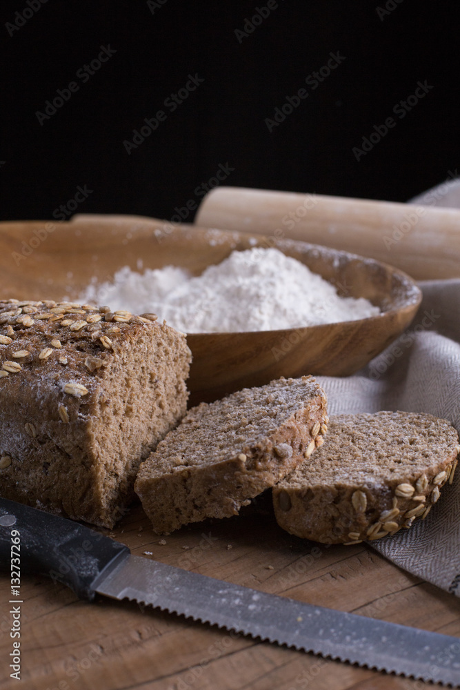 Whole grain wheat bread set on nice fabric brown background decorated with flour bowl and a bakery wooden roller. Whole grain wheat bread set on nice fabric brown background decorated with flour bowl and a bakery wooden roller.