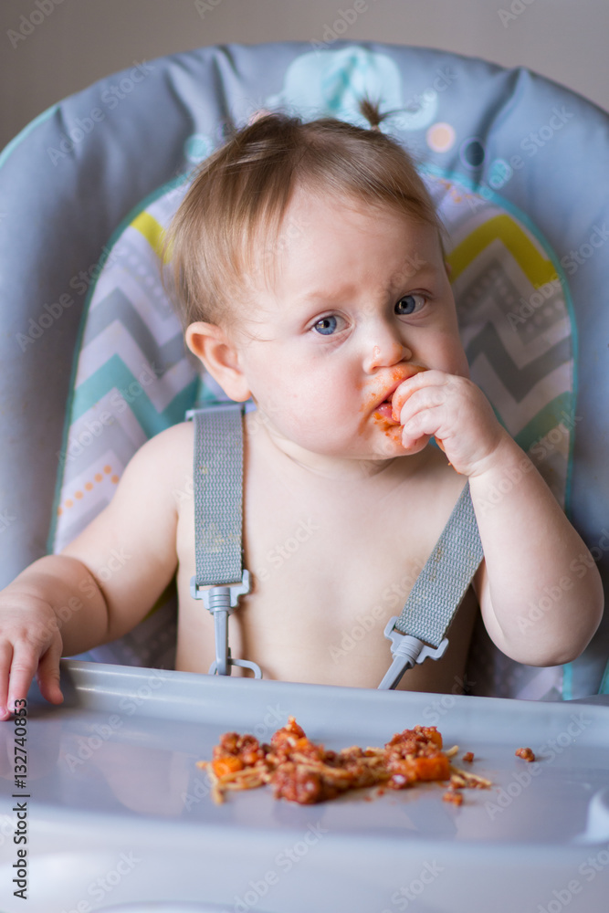 Happy one year old girl eating and enjoying spaghetti while making a mess Happy one year old girl eating and enjoying spaghetti while making a mess