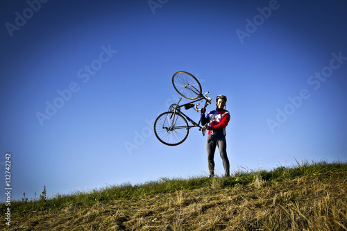 cyclist in the field next to the bicycle standing, holding his bicycle in hands and looking forward for new horizonts on sunny day
