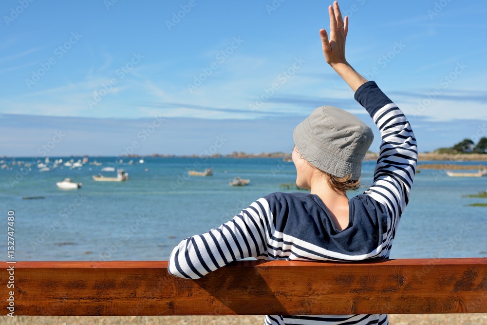 Φωτογραφία Une jeune femme habillée d'un pull marin est assise sur un banc face à la mer