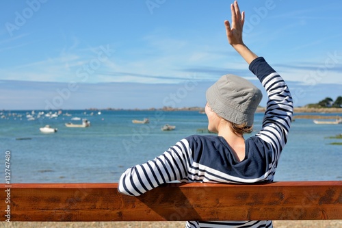 Une jeune femme habillée d'un pull marin est assise sur un banc face à la mer photo
