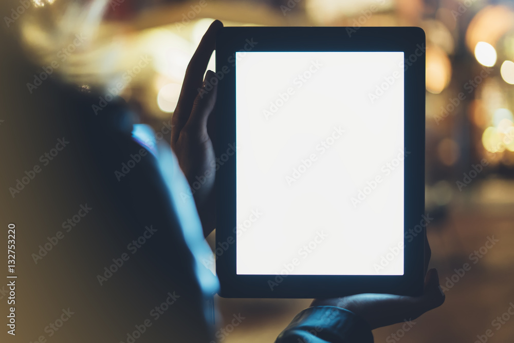 Girl holding in hands on blank screen tablet on background illumination glow bokeh light in night atmospheric christmas city, hands using template mobile computer on lights street; mockup gadget