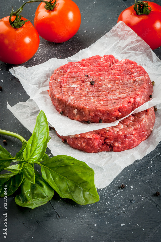 Fresh raw home-made minced beef steak burger with spices, basil and tomatoes on a cutting board on a stone table, copy space, top view Fresh raw home-made minced beef steak burger with spices, basil and tomatoes on a cutting board on a stone table, copy space, top view