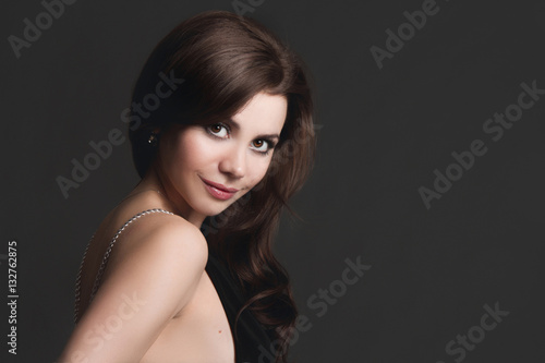 Beautiful sexy girl wearing black evening dress on a gray background. Brunette with charming smile and an open dress