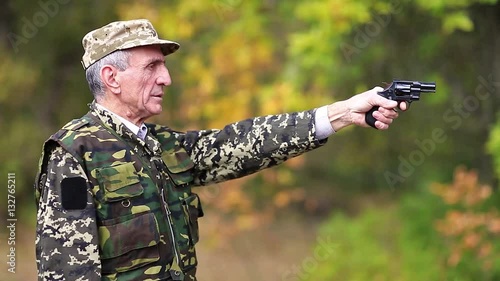 Man with black gun. Senior man in military uniform shoots a revolver. Retired officer at shooting range. Senior man in military uniform shoots a pistol in forest photo