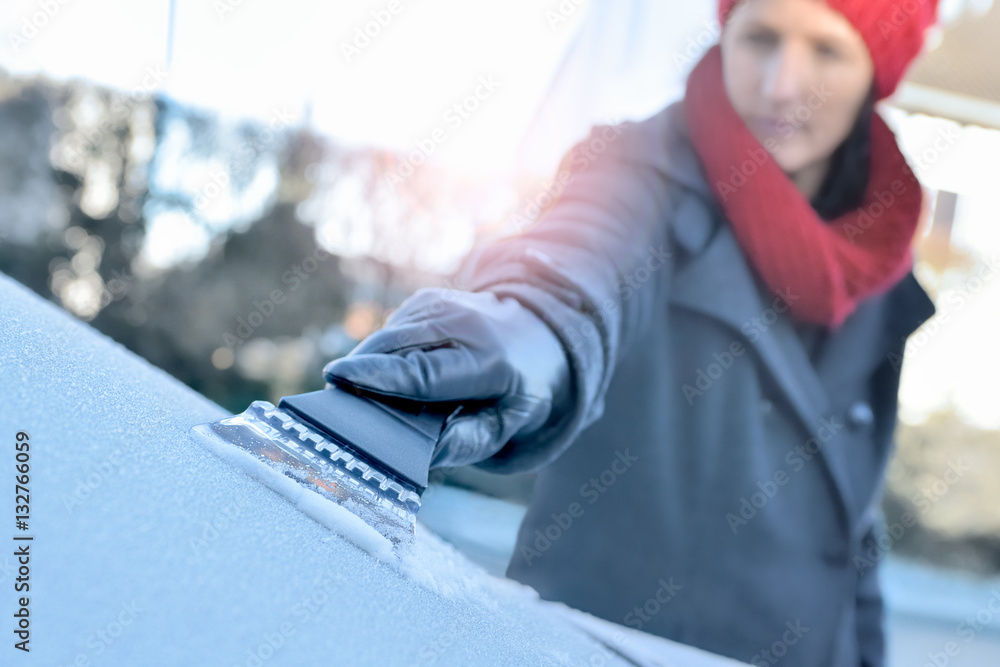 Winter Driving - Woman is scraping Ice from the frozen windows of her car