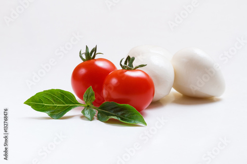 Small mozzarella balls in white bowl with cherry tomatoes and fresh basil on white background