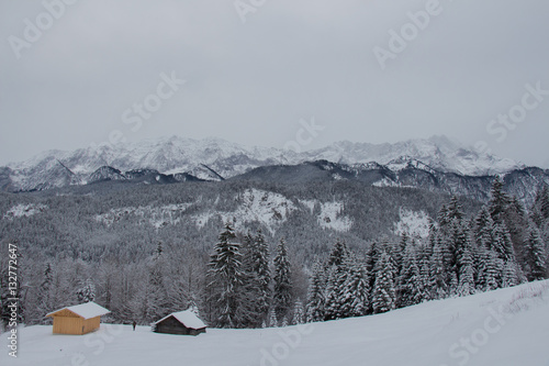 Winter landscape with wooden houses, trees and mountains on background near Garmisch-Partenkirchen. Germany.