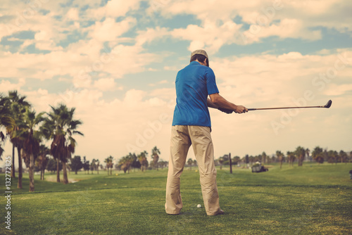 Man holding playing vintage wooden golf club on grass field outdoors background. Back view of active male