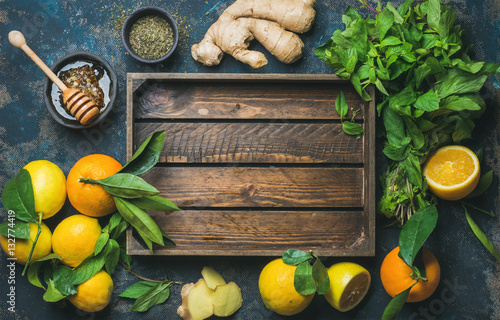 Ingredients for making natural hot drink with wooden tray in center. Oranges, mint, lemons, ginger, honeycomb, apple over plywood background, top view, copy space. Clean eating, detox, dieting concept photo