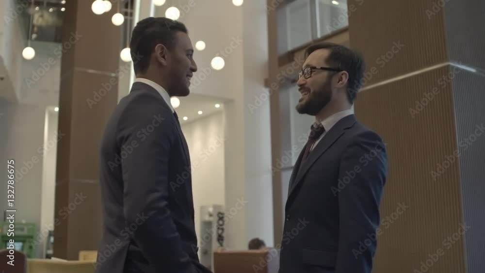 Two businessmen walking towards each other and shaking hands in the office center Two businessmen walking towards each other and shaking hands in the office center