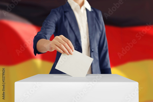Voting. Woman putting a ballot into a voting box with German flag on background.