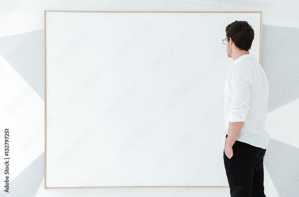Side view of man wearing eyeglasses standing near big board. Side view of man wearing eyeglasses standing near big board.